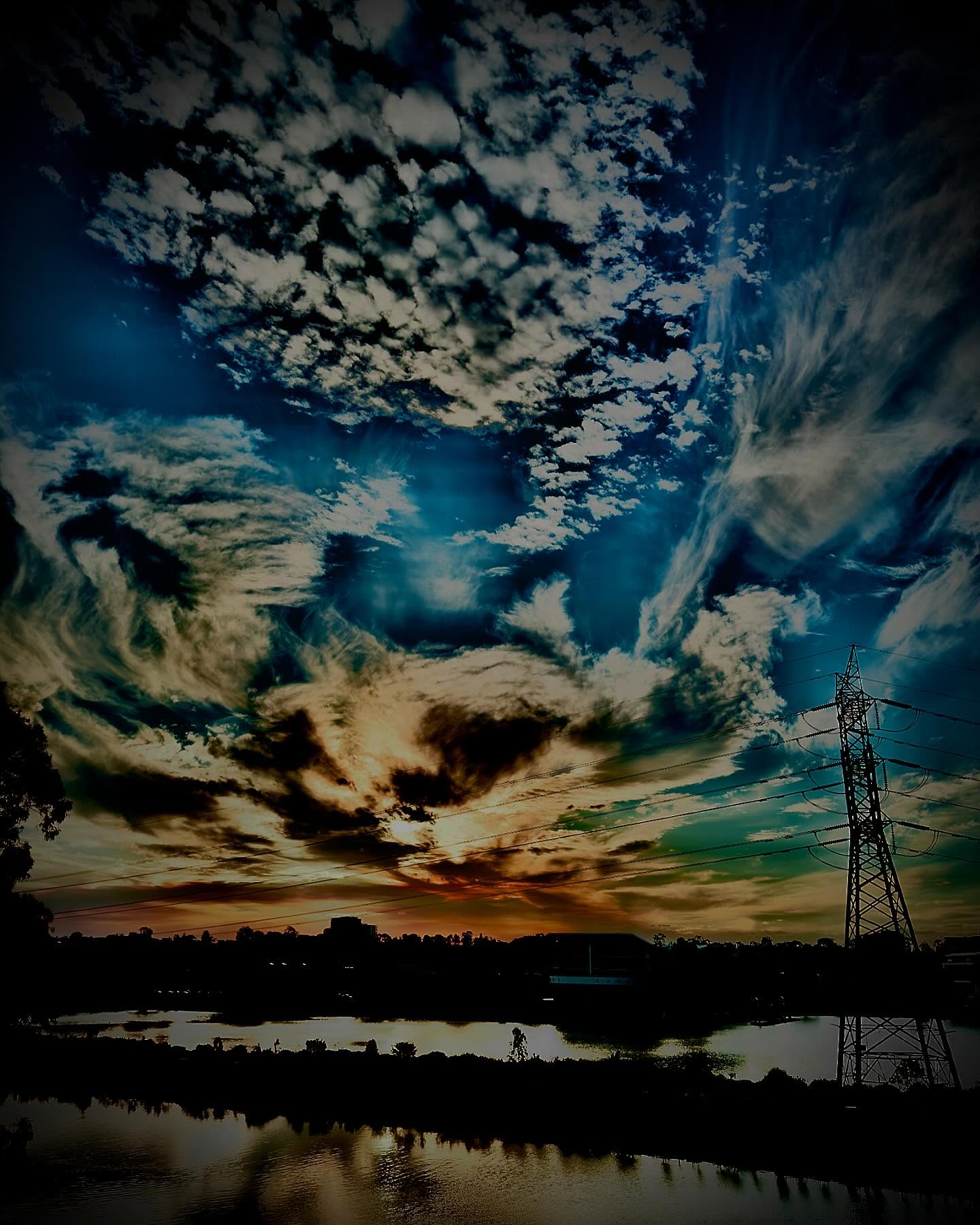 Dramatic Melbourne sky over a dark lake and silhouetted transmission tower