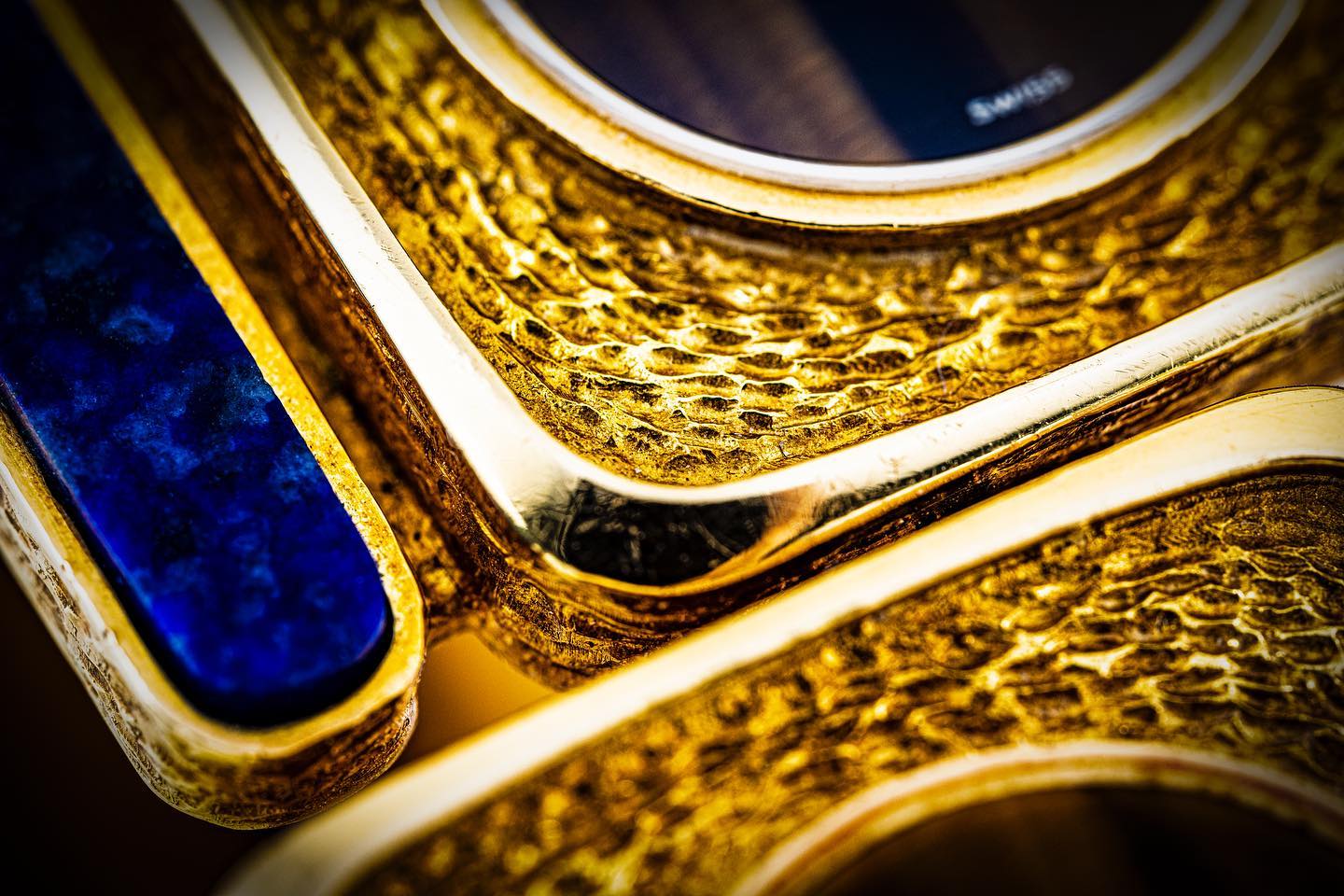 Extreme close-up of a gold watch case with hammered texture and deep blue detail