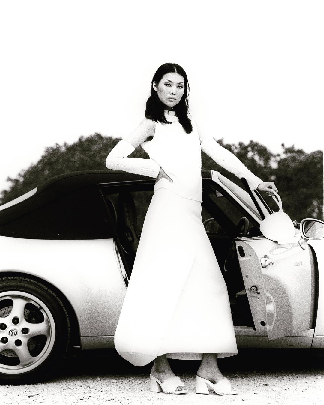 Editorial black-and-white portrait of a model beside a sports car
